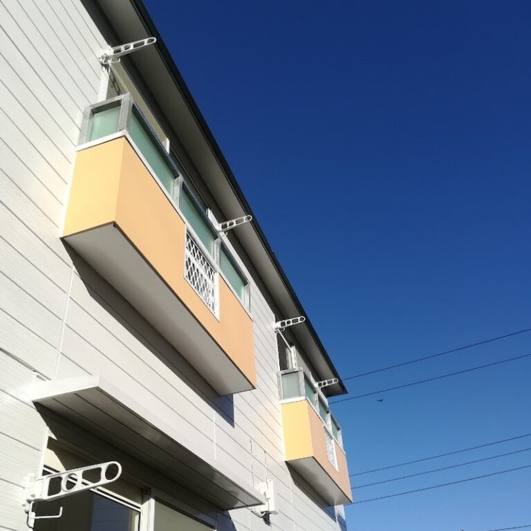 白とオレンジ色のモダンな建物外観。複数の窓とバルコニーが特徴的。
